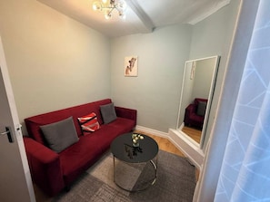 En hyggelig stue med en rød sofa, et rundt sofabord og et spejl.
