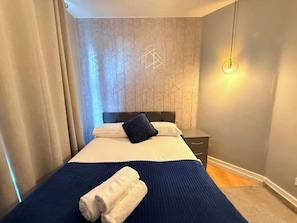 A hotel room with a bed, a nightstand, a lamp, and a wall with a geometric pattern. - Central London Apartment (Greater London)
