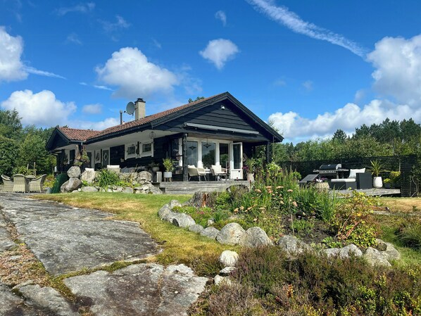 A modern house with a covered porch, stone pathway, and a garden with rocks and plants. - Cottage with terraces on three sides, idyllic isle (Hommersåk)