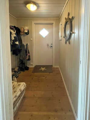 A hallway with a door at the end, a coat rack to the left, and a star-patterned mat on the floor.