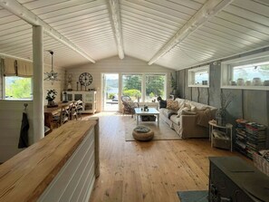 Un vaste espace de vie doté d’un plafond haut, d’un plancher en bois, d’un canapé, d’une table à manger et offrant une vue dégagée grâce à de grandes fenêtres.