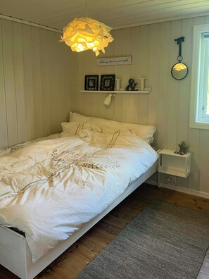 A bedroom with a bed, bedside table, lamp, wall decor, and a window. - Cottage with terraces on three sides, idyllic isle (Hommersåk)