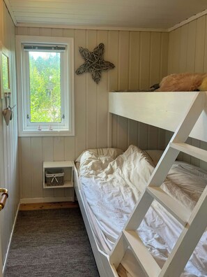 A bunk bed room with a window, a small bedside table, and a wall decoration.
