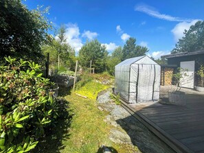 A greenhouse structure with a wooden deck and a garden area with various plants.