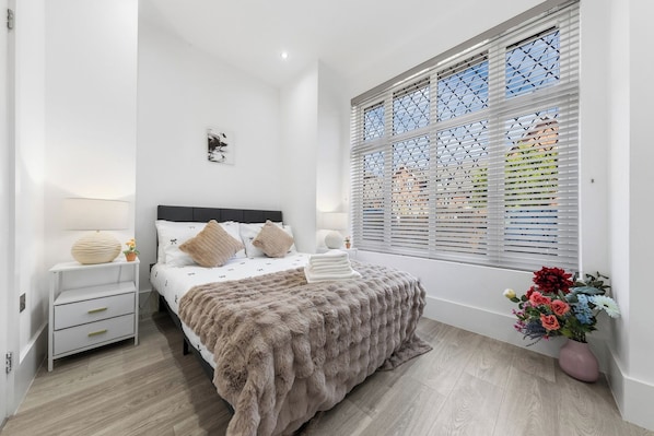 A bedroom with a bed, bedside tables, a window with blinds, and a potted plant. - Harlesden Comfort Studio (Greater London)