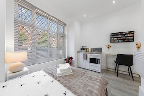 A modern bedroom with a bed, a desk, and a kitchenette. - Harlesden Comfort Studio (Greater London)