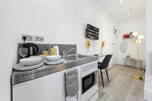 A modern kitchen with a built-in oven, a sink, and a dining area with a chair. - Harlesden Comfort Studio (Greater London)