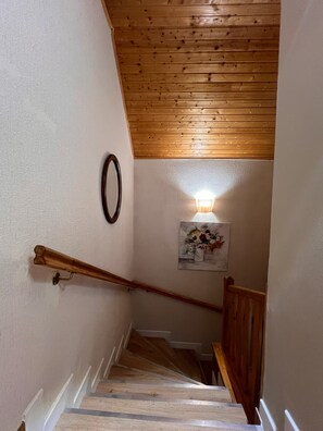 Un escalier en bois avec une rampe, des murs blancs et un plafond avec des poutres apparentes.