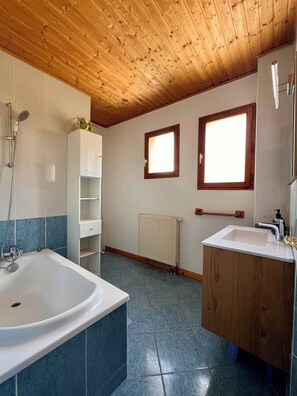 A bathroom with a bathtub, a sink, a window, and a radiator.