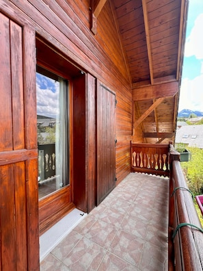 A wooden balcony with a tiled floor, a wooden railing, and a view of the landscape.