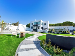 Una casa moderna de dos pisos con un patio, mobiliario exterior y una piscina.