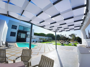 Ein moderner Poolbereich im Freien mit überdachter Terrasse, Liegestühlen und einem Schwimmbecken.