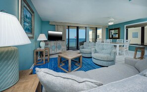 A hotel room with a sofa, armchairs, a TV, a dining table, and a balcony with a view. - Phoenix I 1081 3 Bedroom Condo (Orange Beach)