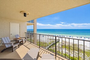 A balcony with a view of a beach, a door, and a table with chairs. - Phoenix I 1061 3 Bedroom Condo (Orange Beach)