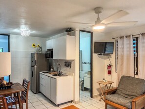 A compact kitchen with a microwave, sink, and cabinets, a dining area with a table and chairs, and a television on the wall.