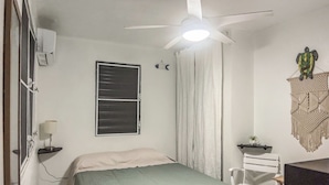 Un dormitorio con cama, ventilador de techo, ventana con persianas, aire acondicionado instalado en la pared, decoración en la pared y un escritorio con silla.