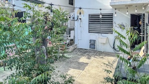 Un patio con una escalera de metal, plantas en macetas y un edificio con varias ventanas y unidades de aire acondicionado.