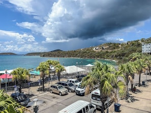 Un estacionamiento frente al mar con vehículos, palmeras y vistas al océano y colinas.