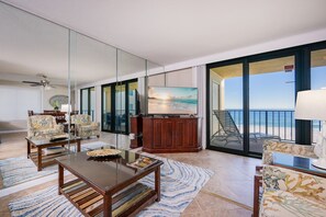 A spacious living area with a large flat-screen TV, a wooden cabinet, and a view of the beach through large sliding glass doors. - Phoenix I 1041 3 Bedroom Condo (Orange Beach)