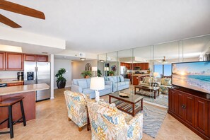A modern living room with a sofa, coffee table, and chairs. There is a kitchen area with a refrigerator and microwave. - Phoenix I 1041 3 Bedroom Condo (Orange Beach)