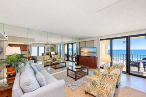 A spacious living room with a large flat-screen TV, comfortable seating, and a view of the ocean through large sliding doors. - Phoenix I 1041 3 Bedroom Condo (Orange Beach)
