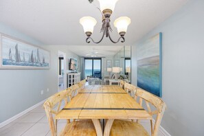 A dining area with a wooden table and chairs, a chandelier, and artwork on the walls. - Phoenix I 1033 2 Bedroom Condo (Orange Beach)