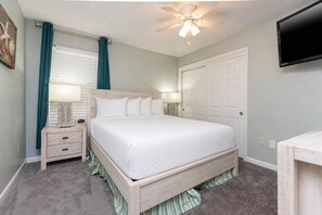 Ein Schlafzimmer mit einem Bett, Nachttischen, einem Deckenventilator, einem Fernseher und einer Tür.