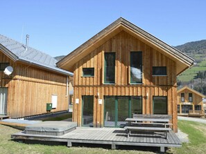 A wooden building with a sloped roof, large windows, and a wooden deck with benches. - One-bedroom Cabin (Sankt Georgen am Kreischberg)