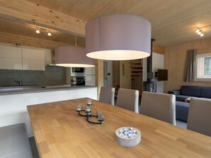 A modern kitchen with white cabinets, a wooden dining table with four chairs, and a large pendant light. - One-bedroom Cabin (Sankt Georgen am Kreischberg)