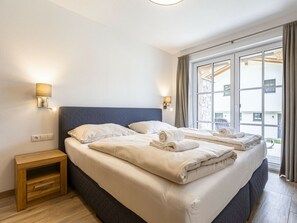Quarto de hotel com cama grande, duas mesas de cabeceira e janela com cortinas.