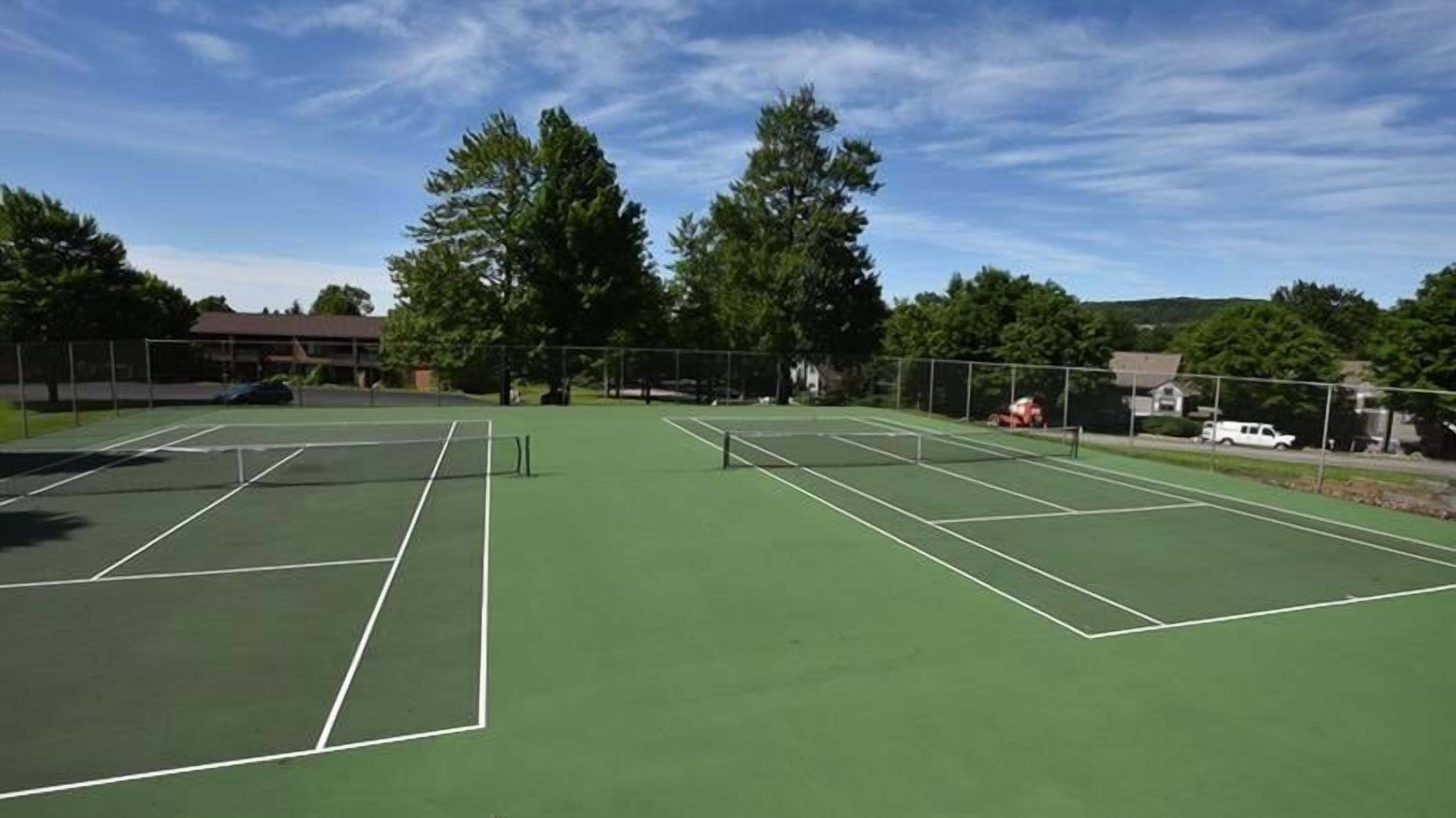 Een tennisbaan met meerdere velden, omgeven door bomen en een heldere lucht.