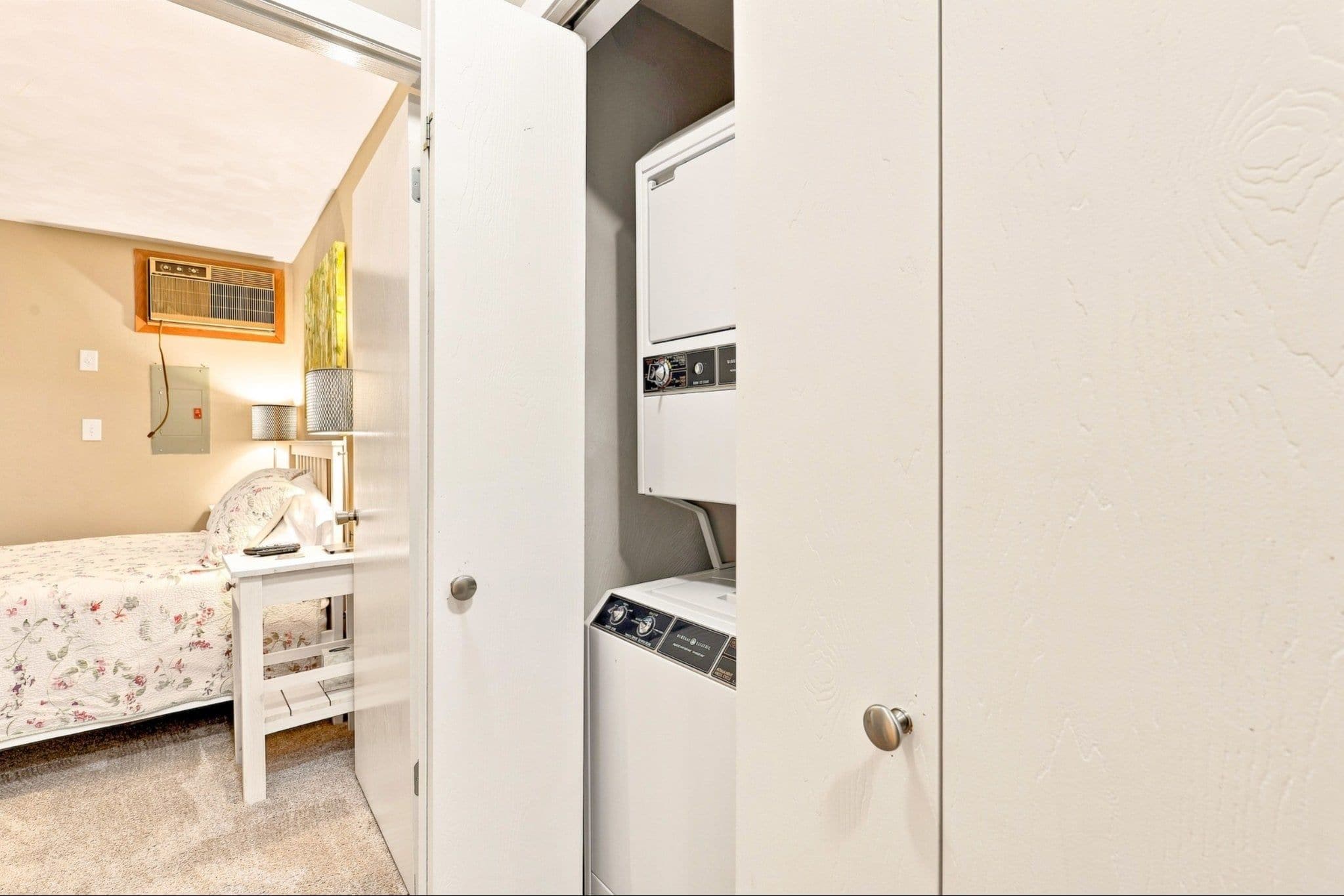 A bedroom with a bed, a nightstand, a lamp, and a wall-mounted heater.