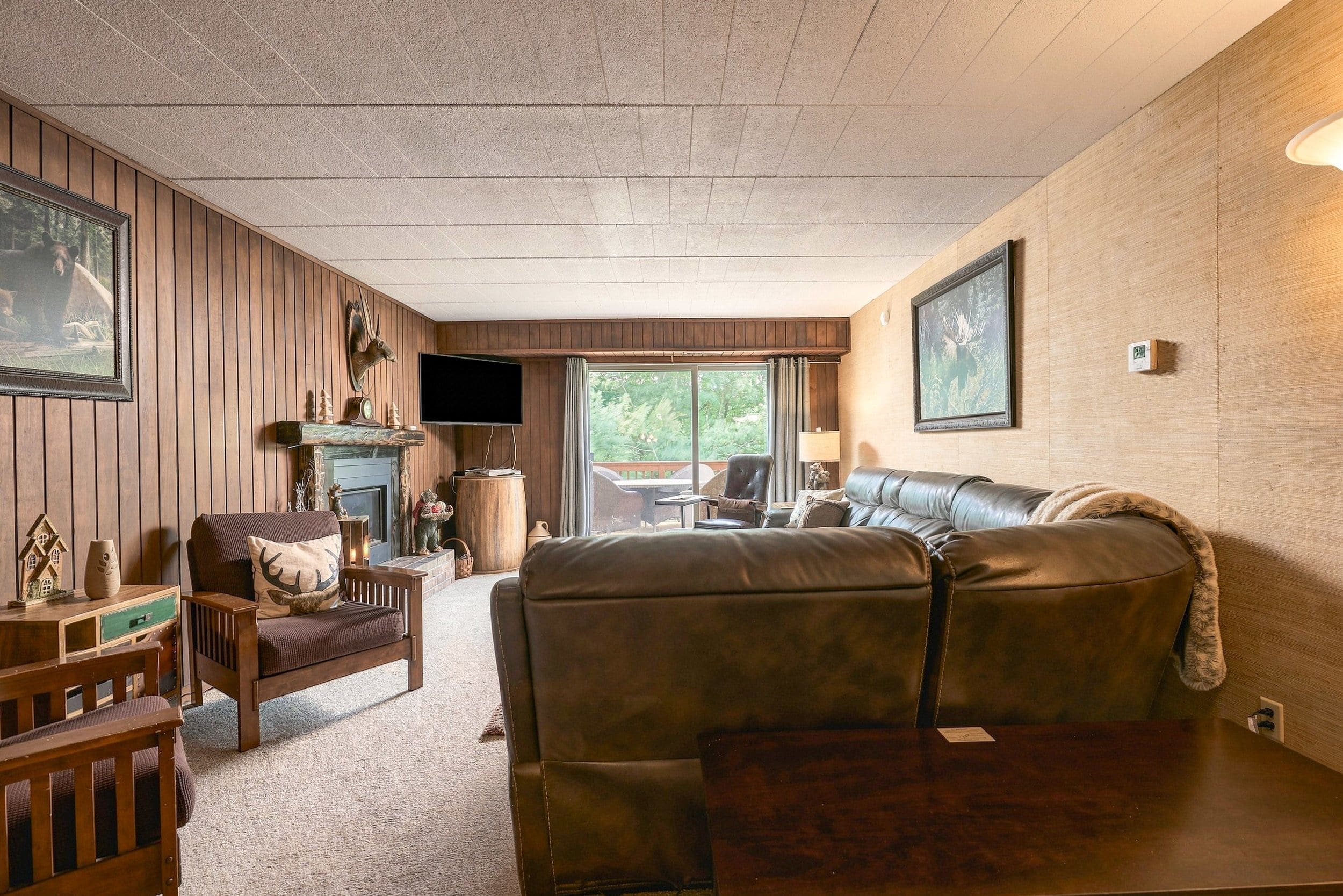 A cozy living room with a leather sofa, wooden furniture, a fireplace, and a television.