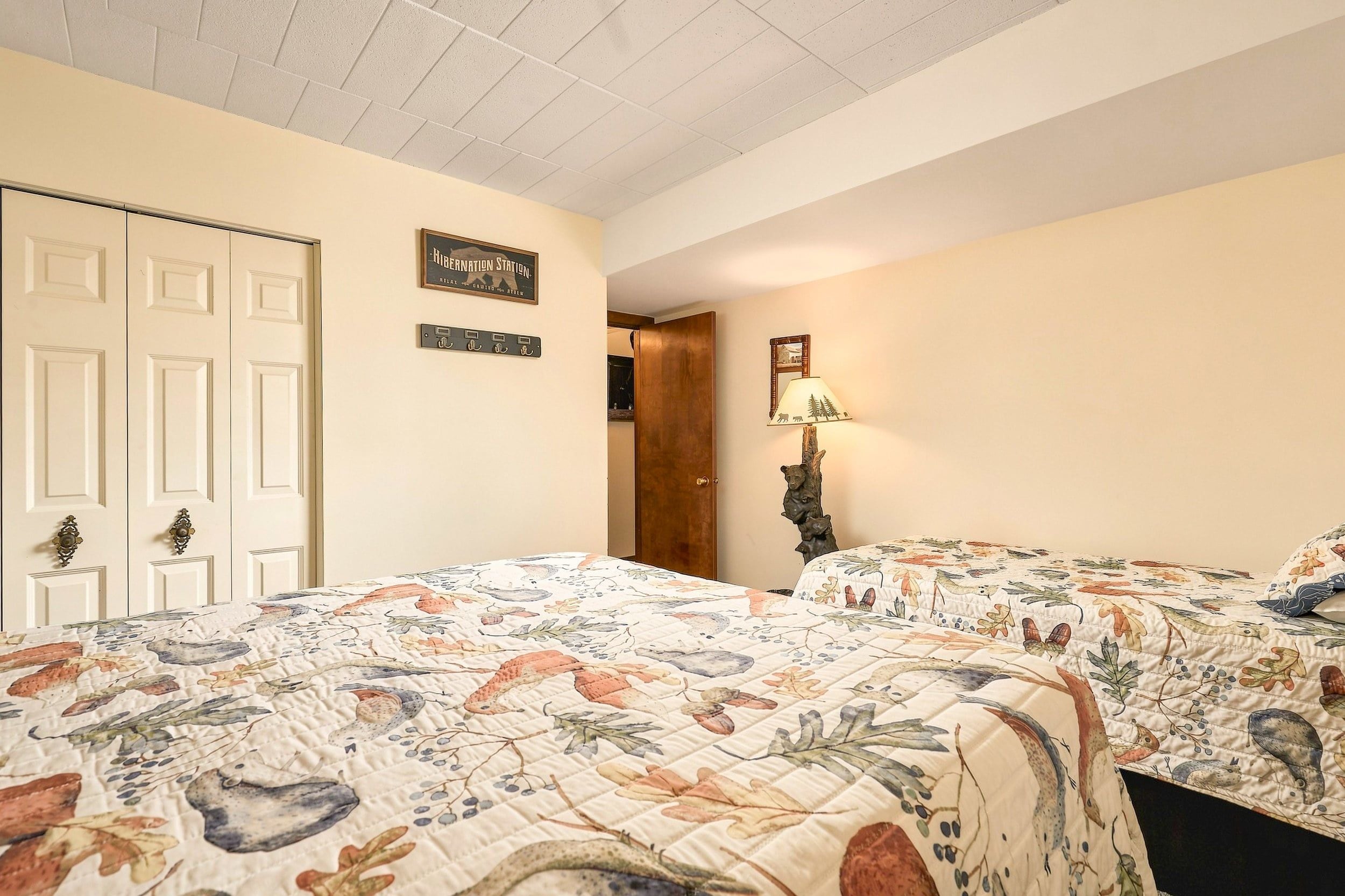 Une chambre avec deux lits, une porte, un luminaire fixé au mur et un tableau encadré.