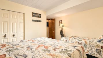 Une chambre avec deux lits, une porte, un luminaire fixé au mur et un tableau encadré.