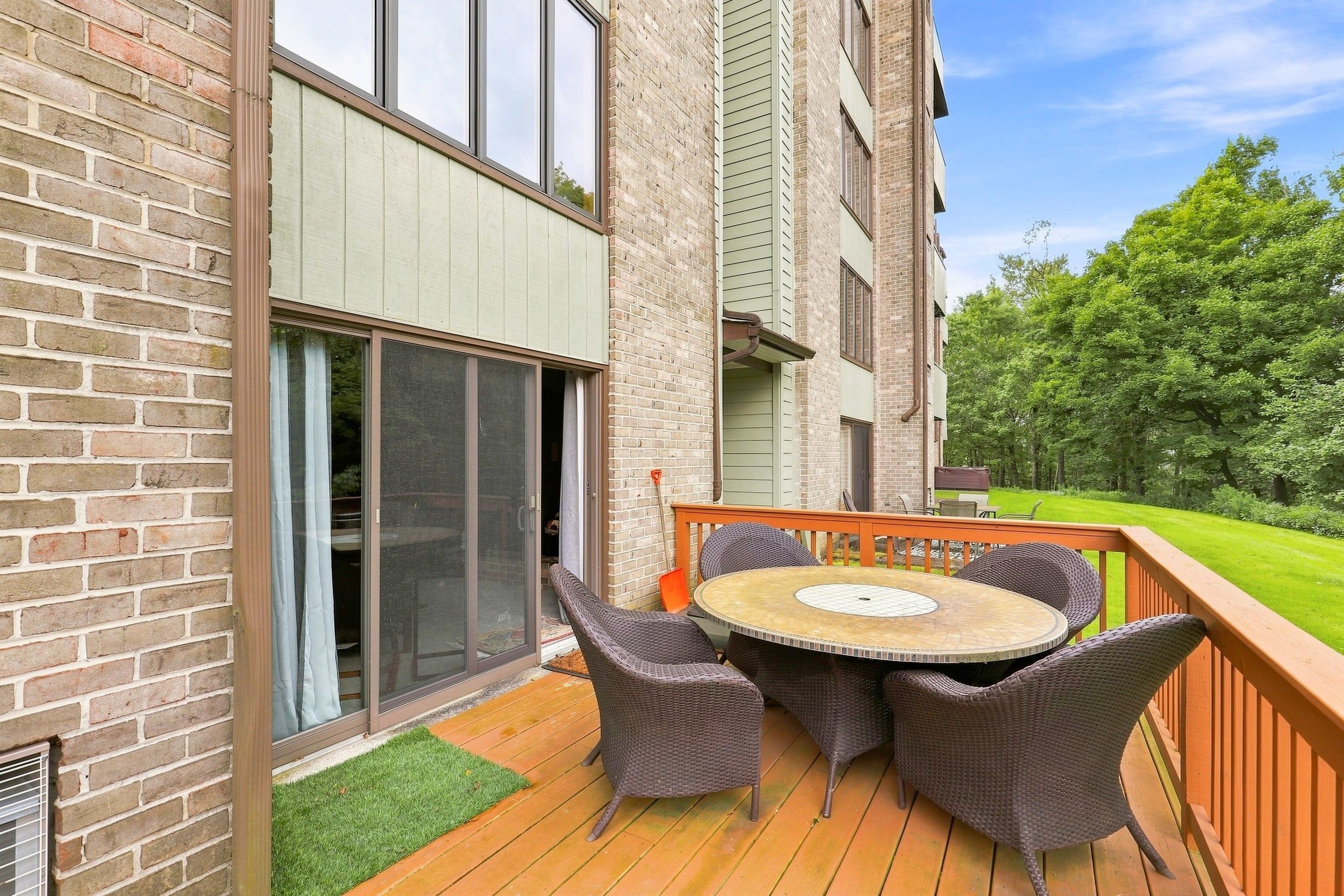 Une terrasse dotée de meubles en osier et d’une table ronde, située à côté d’un bâtiment aux murs en briques et aux grandes fenêtres.