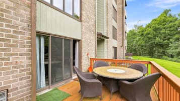 Une terrasse dotée de meubles en osier et d’une table ronde, située à côté d’un bâtiment aux murs en briques et aux grandes fenêtres.