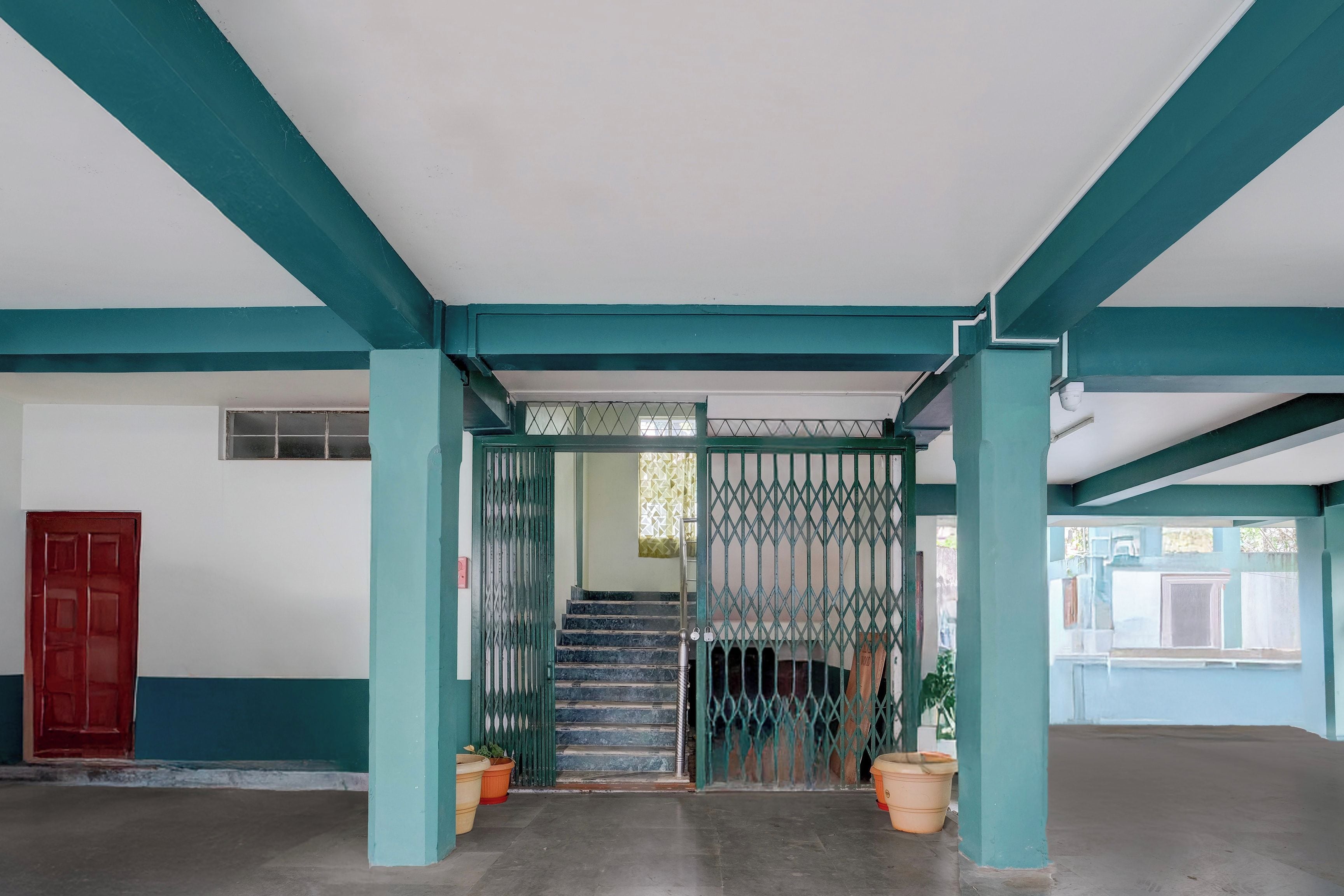 A hallway with teal-colored pillars, a red door, and a gate leading to a staircase.