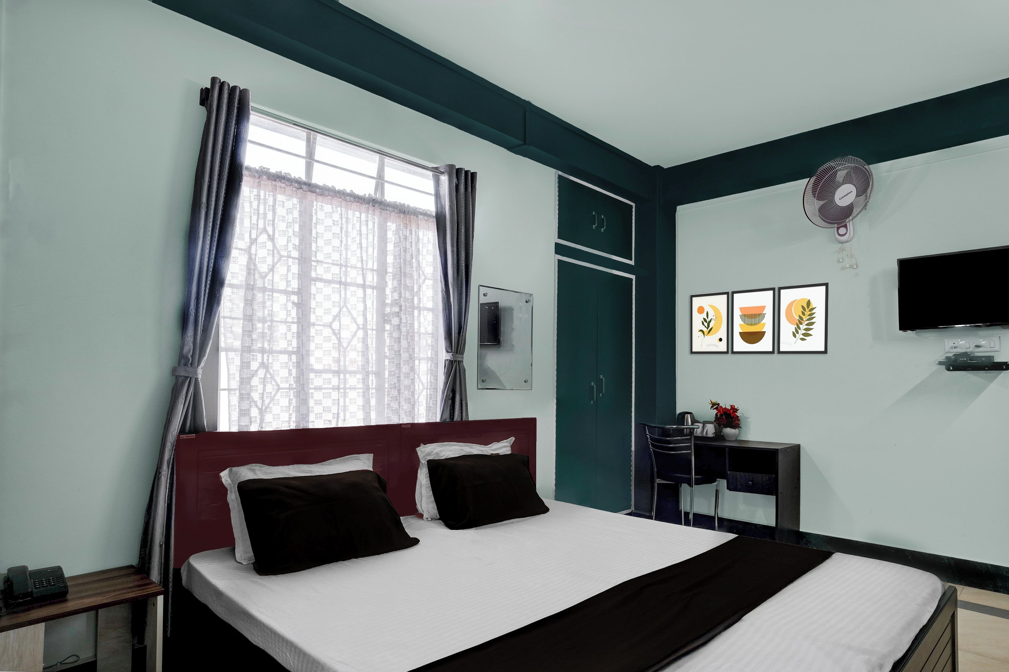 Una habitación de hotel con una cama, un escritorio, una silla, un televisor y obras de arte en la pared.