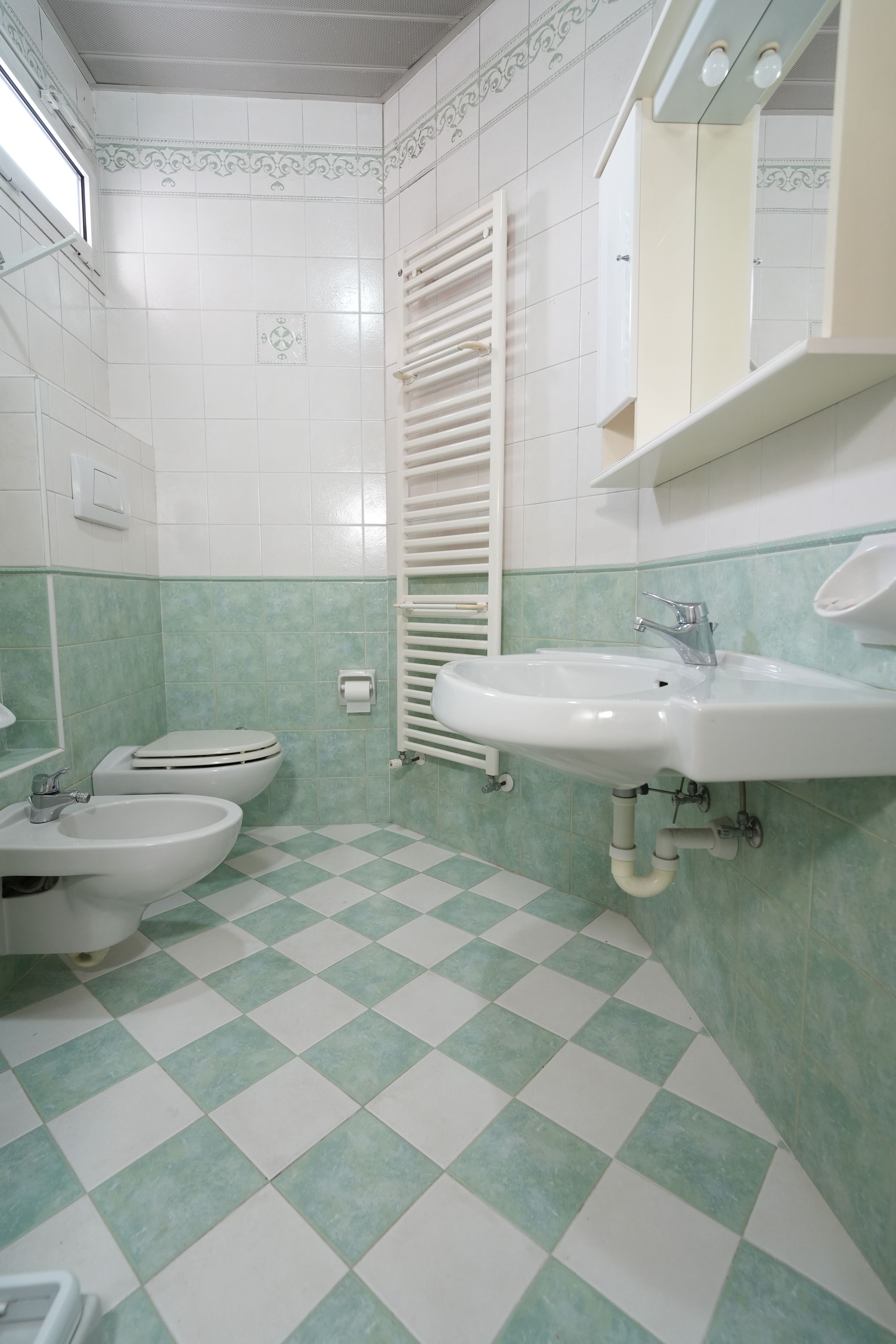 A bathroom with a toilet, bidet, sink, and a towel rack.