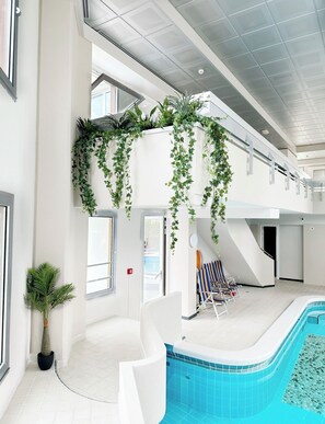 Piscina interior con vista despejada del área de la piscina, una escalera y una zona de estar con sillones de descanso.