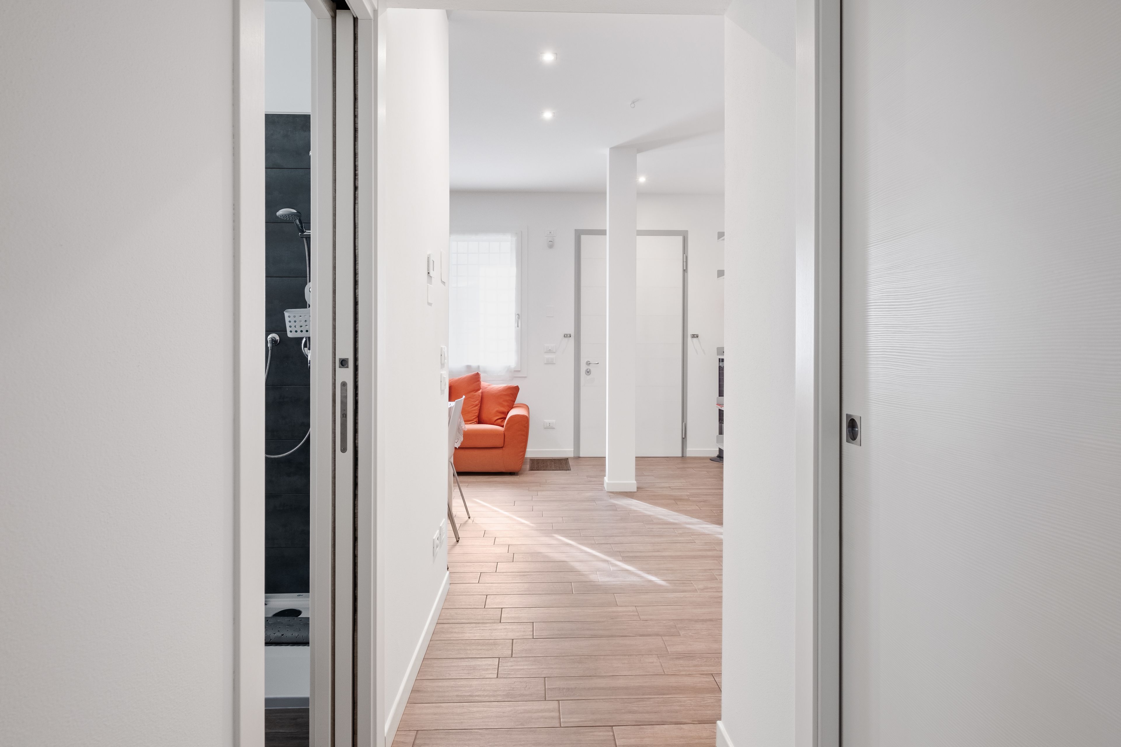 Um interior moderno com piso de madeira, uma porta branca e um quarto iluminado com janela.