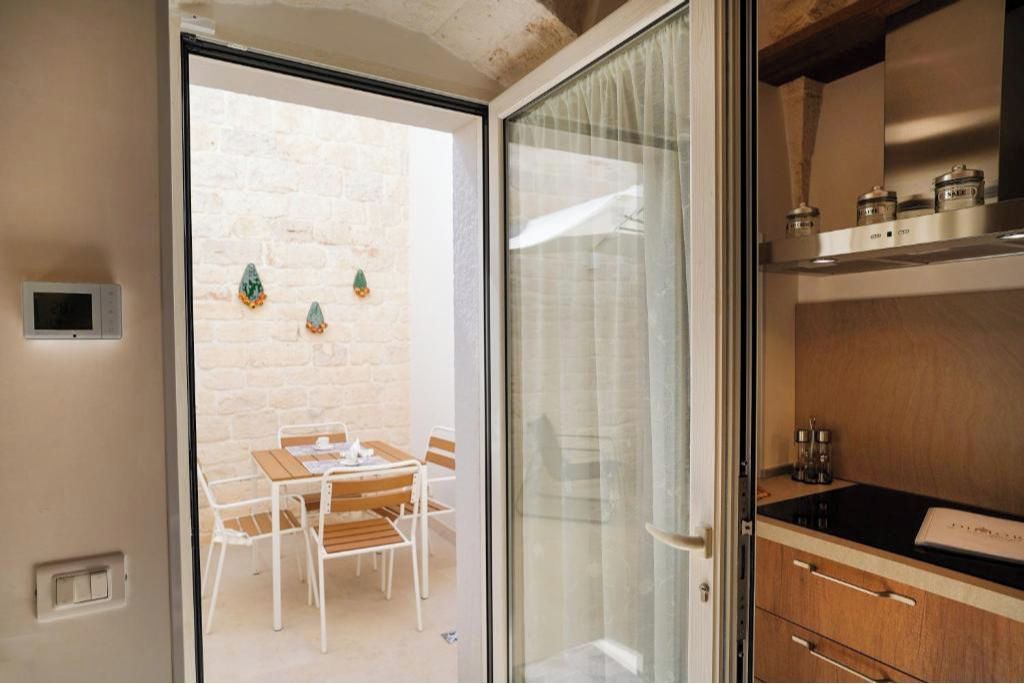 Een moderne keuken met een zwart aanrecht en houten kastjes, een eethoek met een tafel en stoelen, en uitzicht op een bakstenen muur door een glazen deur.