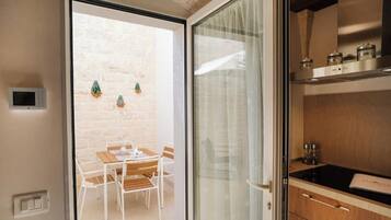 Een moderne keuken met een zwart aanrecht en houten kastjes, een eethoek met een tafel en stoelen, en uitzicht op een bakstenen muur door een glazen deur.