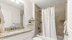 Un baño moderno con encimera de granito, inodoro blanco, ba ñera y cortina de ducha.