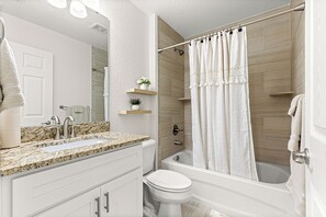 Un baño moderno con encimera de granito, inodoro blanco, bañera y cortina de ducha.