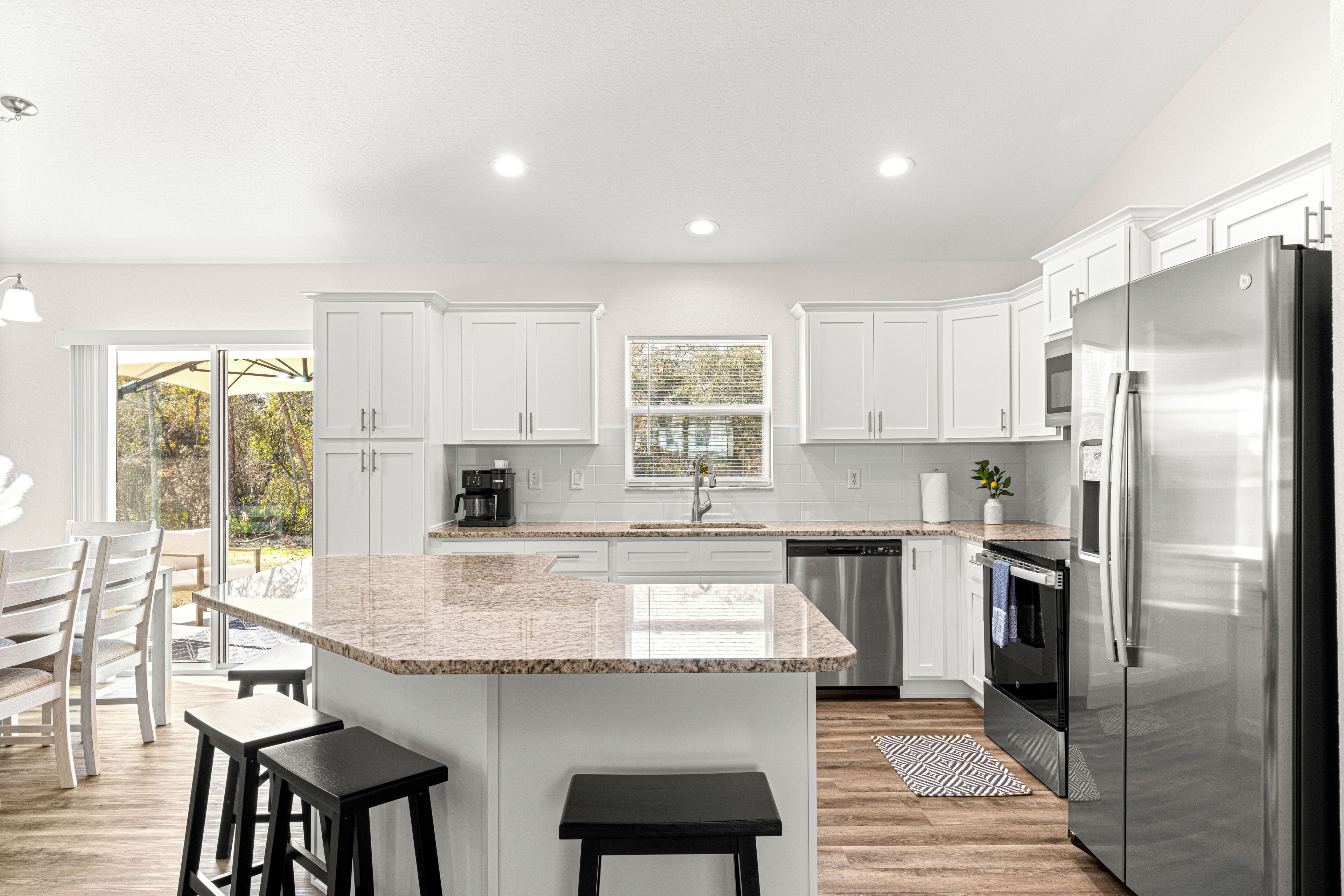 A modern kitchen with white cabinets, a stainless steel refrigerator, and a central island with stools.