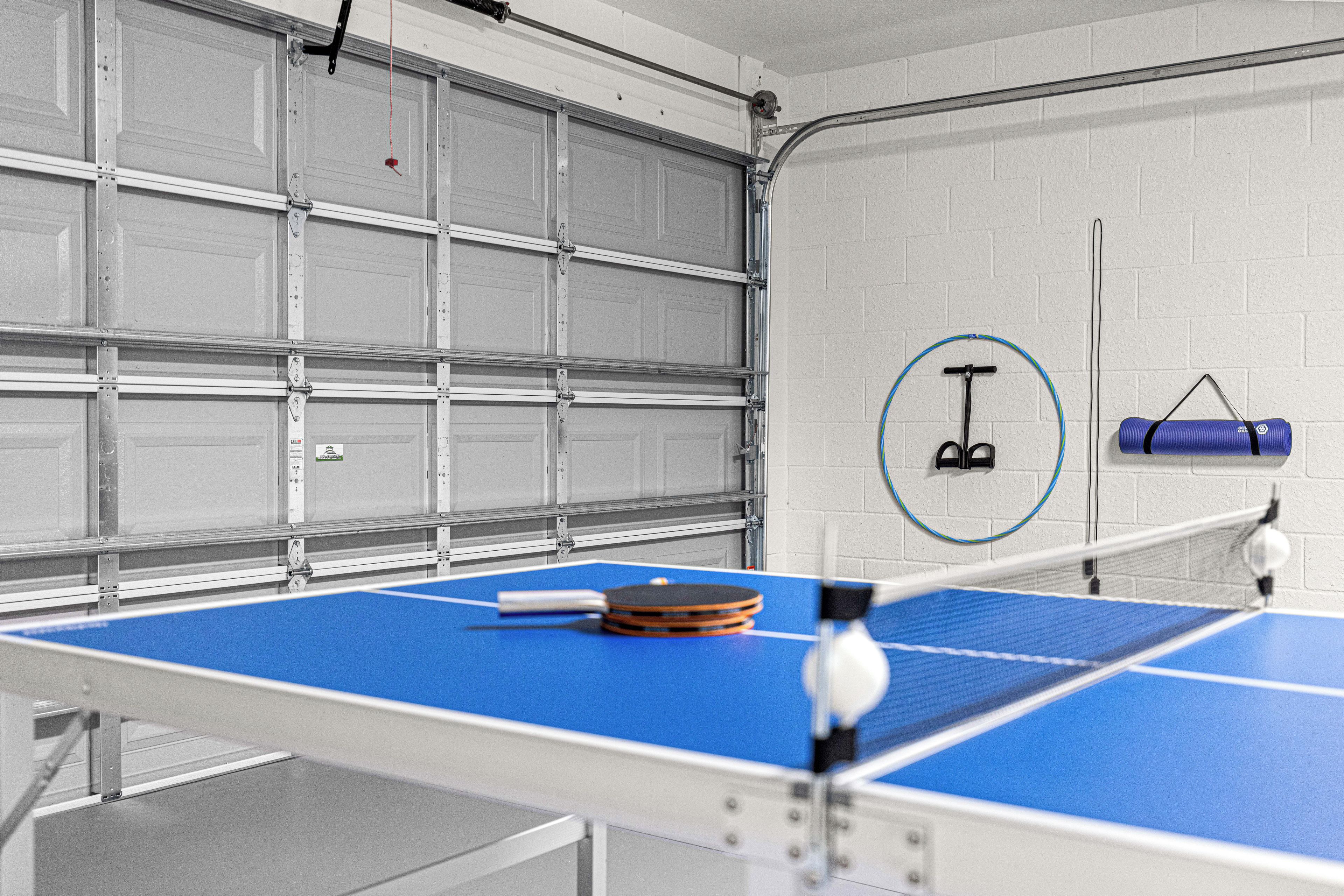 A ping pong table in a garage with a white brick wall and a garage door in the background.