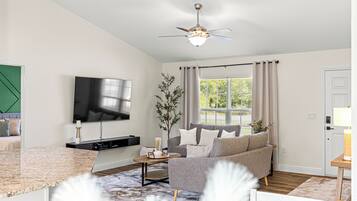A modern living room with a flat-screen TV, a grey sofa, a wooden coffee table, and a ceiling fan.