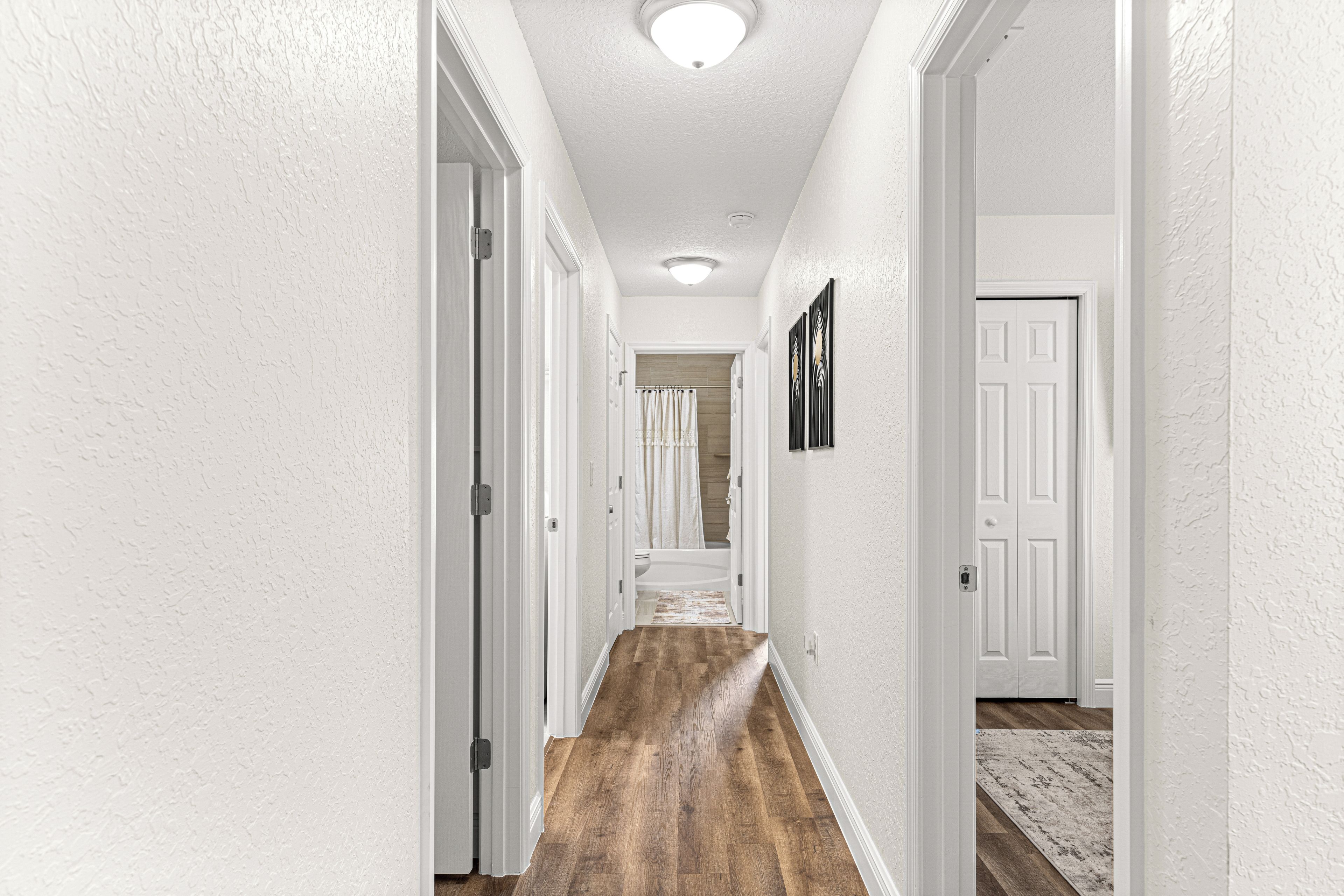 A hallway with white walls, wooden flooring, and white doors.